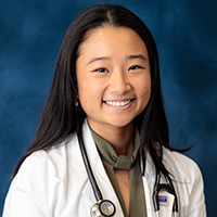 Woman with long, straight dark hair wearing an olive green shirt, white coat with UT Southwestern logo, and stethoscope